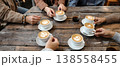 Photo of people enjoying coffee drinks together at a rustic wooden table, fostering connection and conversation in a cafe setting. 138558455