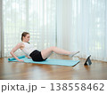 Young woman doing core exercise at home on yoga mat. Concept of fitness, strength training, and online workout. Female performing leg raise while following virtual fitness class. 138558462