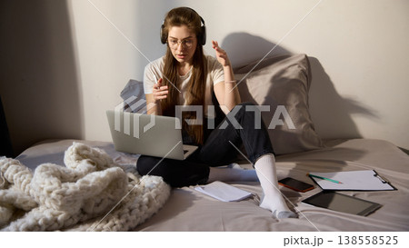 Young woman with headphones learning on laptop while sitting on bed at home. Young woman with headphones learning on laptop while sitting on bed at home. 138558525
