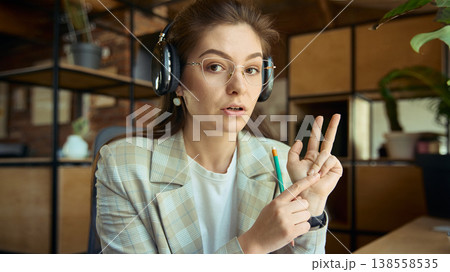 Woman with headphones explaining counting on fingers during online coaching. 138558535