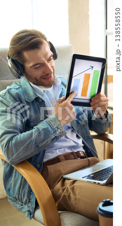 Man with headphones showing growth chart on tablet during online coaching. 138558550