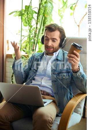 Man with headphones holding coffee cup talking during online coaching session 138558554