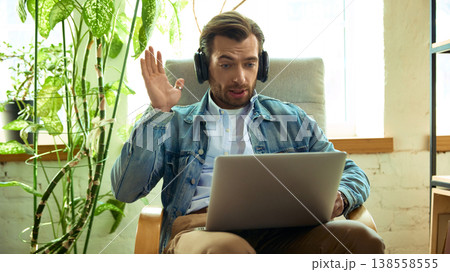 Man with headphones reacting surprised during online coaching call on laptop. 138558555