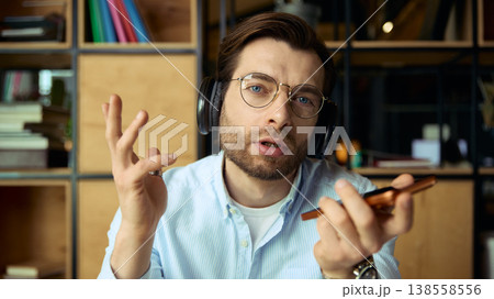 Man with headphones speaking on smartphone during online coaching session 138558556