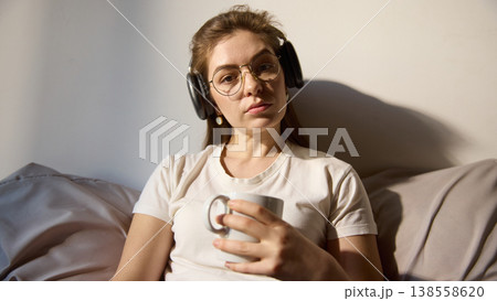 Young woman holding cup and looking at camera during online lesson at home. Young woman holding cup and looking at camera during online lesson at home. 138558620