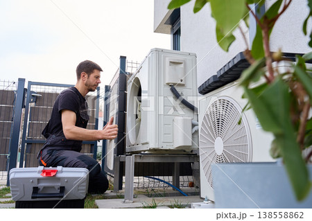 Technician servicing outdoor air source heat pump unit near house wall 138558862
