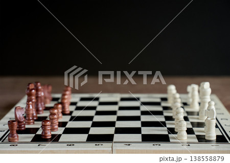 Chessboard with white and brown pieces against dark background Chessboard with white and brown pieces against dark background 138558879