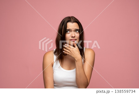 Young woman feeling doubt and uncertainty, looking away with worried expression on pink background Young woman feeling doubt and uncertainty, looking away with worried expression on pink background 138559734