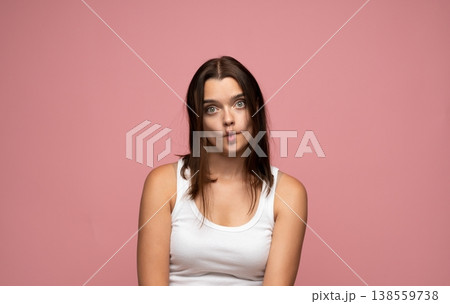 Young woman making a funny face with fish lips on a pink background, expressing playfulness and humor Young woman making a funny face with fish lips on a pink background, expressing playfulness and humor 138559738