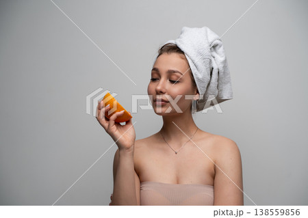 Young woman with a towel-wrapped head showcasing natural beauty and self-care, holding an orange slice embodying fresh ingredients and vitamin C for radiant skin Young woman with a towel-wrapped head showcasing natural beauty and self-care, holding an orange slice embodying fresh ingredients and vitamin C for radiant skin 138559856