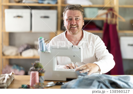 Happy middle-aged male dressmaker working with sewing-machine Happy middle-aged male dressmaker working with sewing-machine 138560127