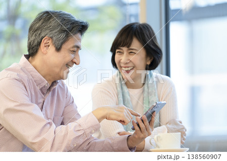カフェでスマートフォンを見ながら話をする60代の夫婦　 138560907