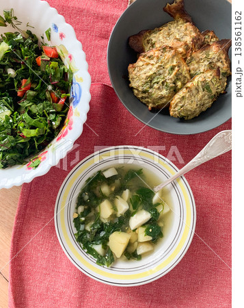 A bowl of green nettle soup with potatoes sits on a table alongside a fresh salad and vegetable pancakes. It is a simple meal enjoyed during a warm afternoon A bowl of green nettle soup with potatoes sits on a table alongside a fresh salad and vegetable pancakes. It is a simple meal enjoyed during a warm afternoon 138561162