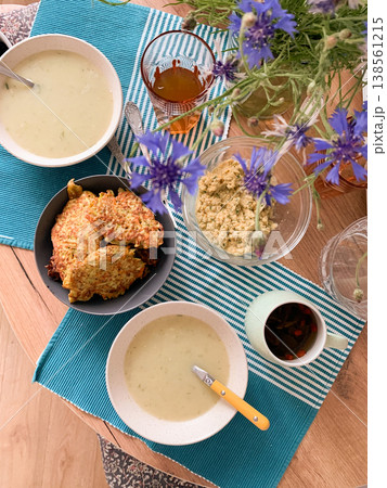 Two bowls of cream of cauliflower soup sit on a table along with a bowl of boiled vegetable salad and vinaigrette. Drinks and flowers add to the scene Two bowls of cream of cauliflower soup sit on a table along with a bowl of boiled vegetable salad and vinaigrette. Drinks and flowers add to the scene 138561215