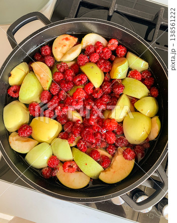Green apples and red raspberries are placed in a pot on the stove. The fruits are prepared for cooking to make a sweet compote. This happens in a kitchen 138561222
