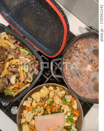 Vegetables are simmering in a pan while meat fries in another. Lentil soup is cooking in a pot, creating a balanced meal for breakfast or lunch in the kitchen 138561242