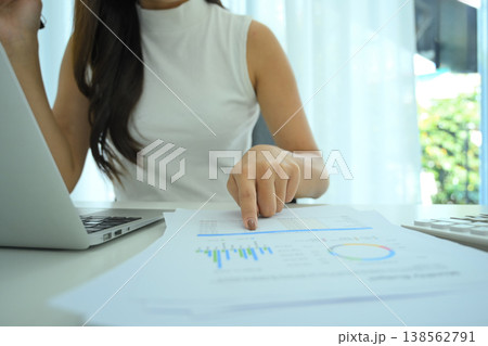 Wide angle photo of woman pointing to financial chart on printed report while working on laptop Wide angle photo of woman pointing to financial chart on printed report while working on laptop 138562791