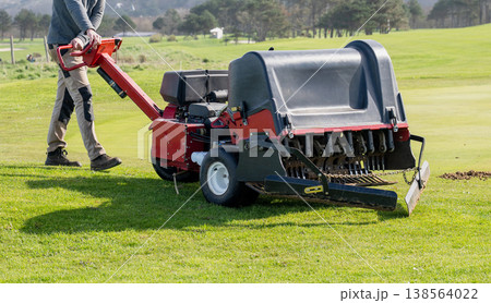 Groundskeeper aerating golf course green with professional turf maintenance machine on sunny day sports field care concept Groundskeeper aerating golf course green with professional turf maintenance machine on sunny day sports field care concept 138564022