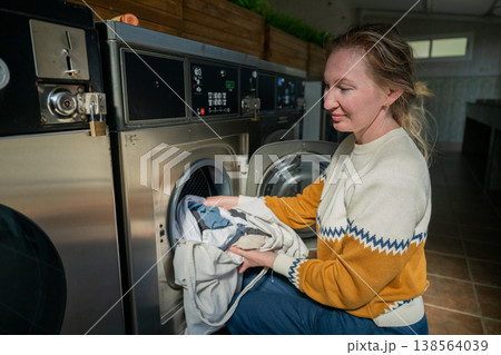 Woman loading laundry into washing machine at modern self service laundromat interior lifestyle scene 138564039