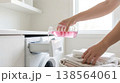 Person pours laundry detergent from bottle into washing machine drawer. Bright laundry room with clean towels folded on countertop. Concept of cleaning, home care, laundry service. 138564061