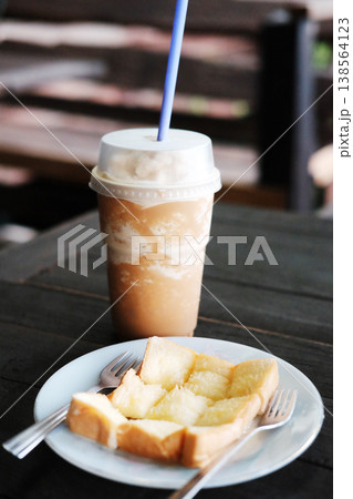 Homemade toast or bread with butter topping in white dish with blended latte coffee in plastic glass on wooden table Homemade toast or bread with butter topping in white dish with blended latte coffee in plastic glass on wooden table 138564123