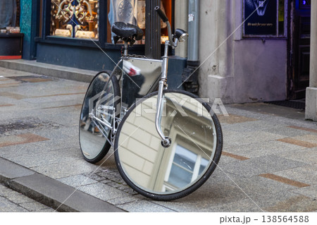 Distinctive mirrored bicycle with highly reflective wheels and frame, parked on a textured urban sidewalk, showcasing innovative design and street art 138564588