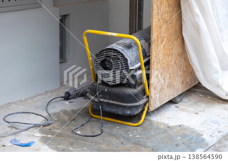 Powerful industrial space heater with a yellow frame, actively drying a concrete floor on a bustling construction site for efficient building renovation Powerful industrial space heater with a yellow frame, actively drying a concrete floor on a bustling construction site for efficient building renovation 138564590