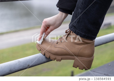 Woman's hand meticulously cleans a sturdy brown leather boot using a white disposable wipe, highlighting practical outdoor shoe care and proactive footwear maintenance Woman's hand meticulously cleans a sturdy brown leather boot using a white disposable wipe, highlighting practical outdoor shoe care and proactive footwear maintenance 138564593