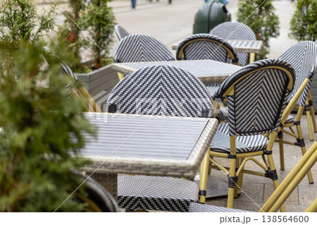 Stylish outdoor cafe furniture featuring patterned black and white chairs, modern tables, ready for urban sidewalk dining, promoting relaxed leisure 138564600