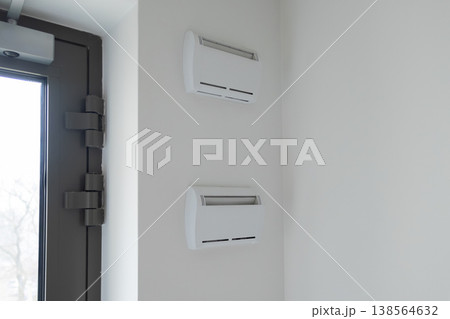 Two modern white climate control units are mounted vertically on a light wall, suggesting efficient temperature management in a contemporary office or public building 138564632