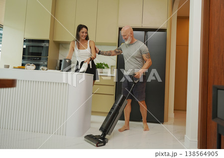 Man with woman vacuuming in modern sunlight kitchen. Man with woman vacuuming in modern sunlight kitchen. 138564905