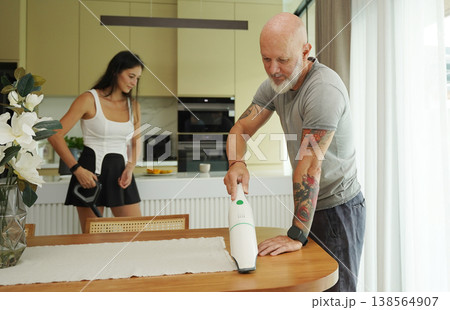 Man with woman vacuuming in modern sunlight kitchen. Man with woman vacuuming in modern sunlight kitchen. 138564907