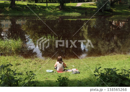 Calm woman unwinding next to tranquil river during sunny afternoon 138565268