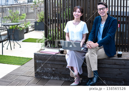 リモートワーク中に屋外でコーヒーを飲みながら会話を楽しむ若い男女 138565526