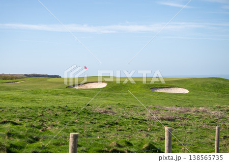 Golf course green with sand bunker and red flag on coastal landscape under blue sky Golf course green with sand bunker and red flag on coastal landscape under blue sky 138565735