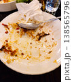 Eaten dish rests on a white plate. Spoon lies idle beside crumpled napkin. Residue hints at rich, savory flavor. Dark table surface adds moody contrast. Perfect for food review or post-dining scenes 138565796