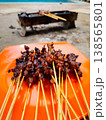 Grilled skewers sizzle on a bright orange plate. Fragrant meat glows with smoky, charred perfection. Background shows a rustic barbecue cart. Cozy beachside meal evokes warmth and hunger 138565801