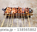 Skewers of grilled meat sizzle over hot coals. Smoke curls upward from the fiery grill. Each piece glistens with savory, charred flavor. The scene radiates warmth and appetite 138565802