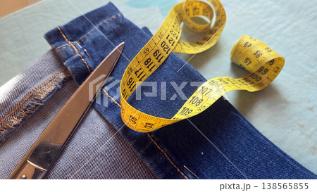 Closeup of denim jeans with scissors and coiled yellow measuring tape for tailoring background and clothing repair design 138565855