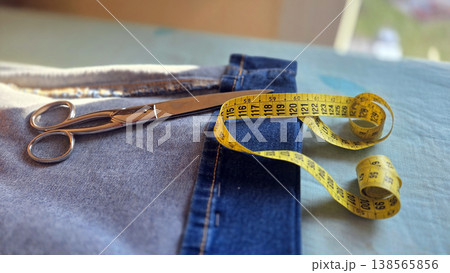 Flatlay of denim jeans with sharp scissors and yellow measuring tape for tailoring background and alteration workshop design 138565856
