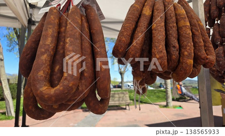 Long cured chorizo links hanging in bunches at an outdoor spanish farmers market for deli display background and traditional food banner Long cured chorizo links hanging in bunches at an outdoor spanish farmers market for deli display background and traditional food banner 138565933