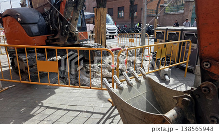 Orange excavator at urban construction site with bucket and safety barriers for background and banner design for roadwork projects Orange excavator at urban construction site with bucket and safety barriers for background and banner design for roadwork projects 138565948