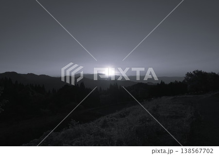 モノクロの山並みと光る夕日のシルエット 138567702
