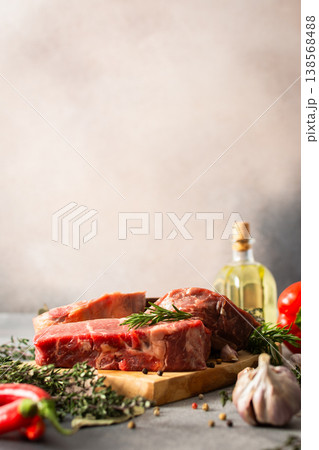 A piece of beef steak rests on a wooden cutting board with herbs and spices. The setting shows a work area in the kitchen where food preparation occurs A piece of beef steak rests on a wooden cutting board with herbs and spices. The setting shows a work area in the kitchen where food preparation occurs 138568488