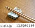 木目調のテーブルの上に置かれた猫のイラストが描かれた白い陶器の箸置きと木の箸 138569136