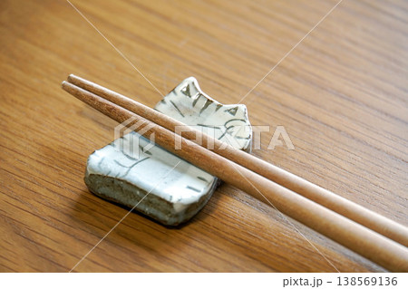 木目調のテーブルの上に置かれた猫のイラストが描かれた白い陶器の箸置きと木の箸 138569136