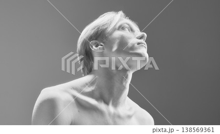 High contrast portrait of young man with upward pose in minimal studio lighting. 138569361