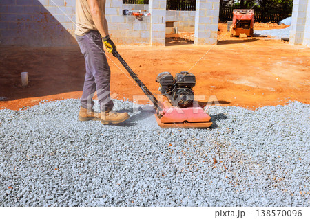 Worker operates plate compactor on gravel at construction site 138570096