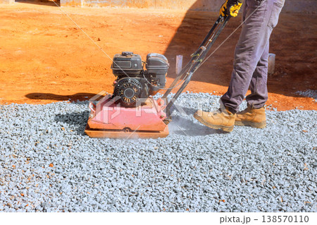 Worker operates machine gravel compactor to compress gravel on construction site Worker operates machine gravel compactor to compress gravel on construction site 138570110