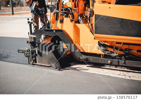Asphalt paving large machine is laying fresh asphalt on road while workers oversee process 138570117